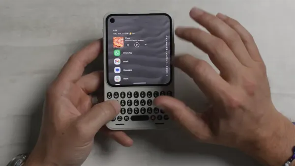 Clicks Communicator tenuto in mano: si vedono lo schermo con le app e la tastiera fisica QWERTY