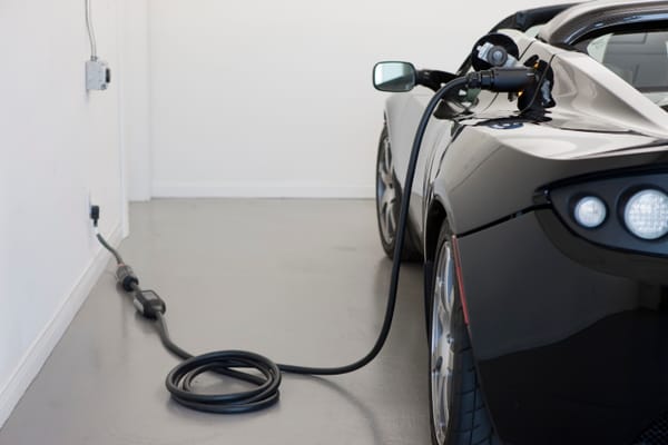Tesla Roadster scuro in ricarica, collegato a una presa a muro